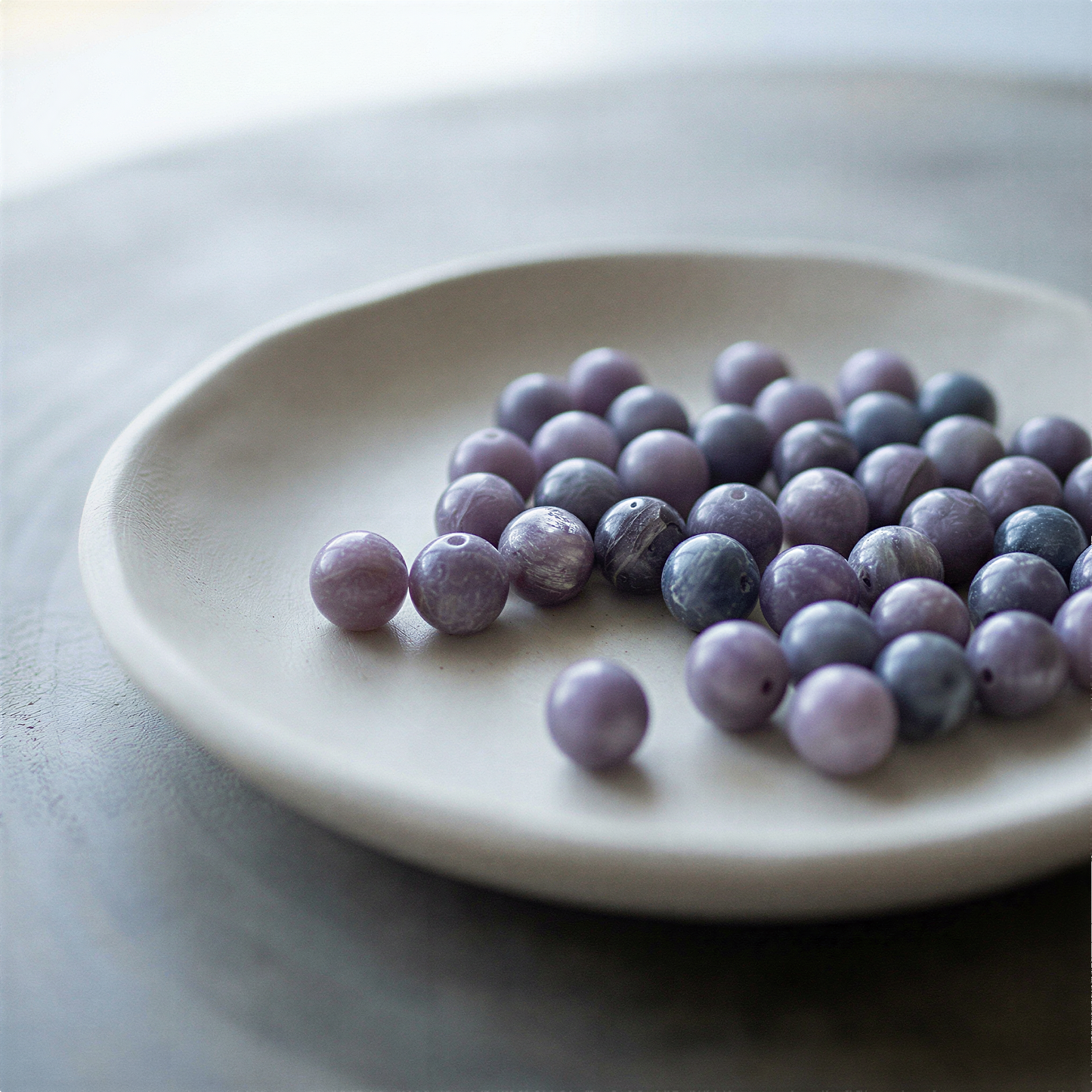 Single purple lepidolite 8mm bead resting on natural stone surface in soft, diffused daylight