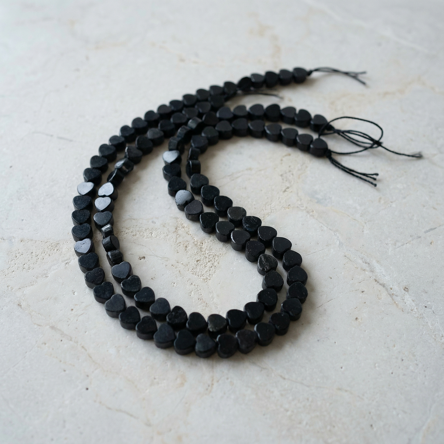 Black tourmaline heart bead strand resting on raw stone with diffused daylight and desert textures