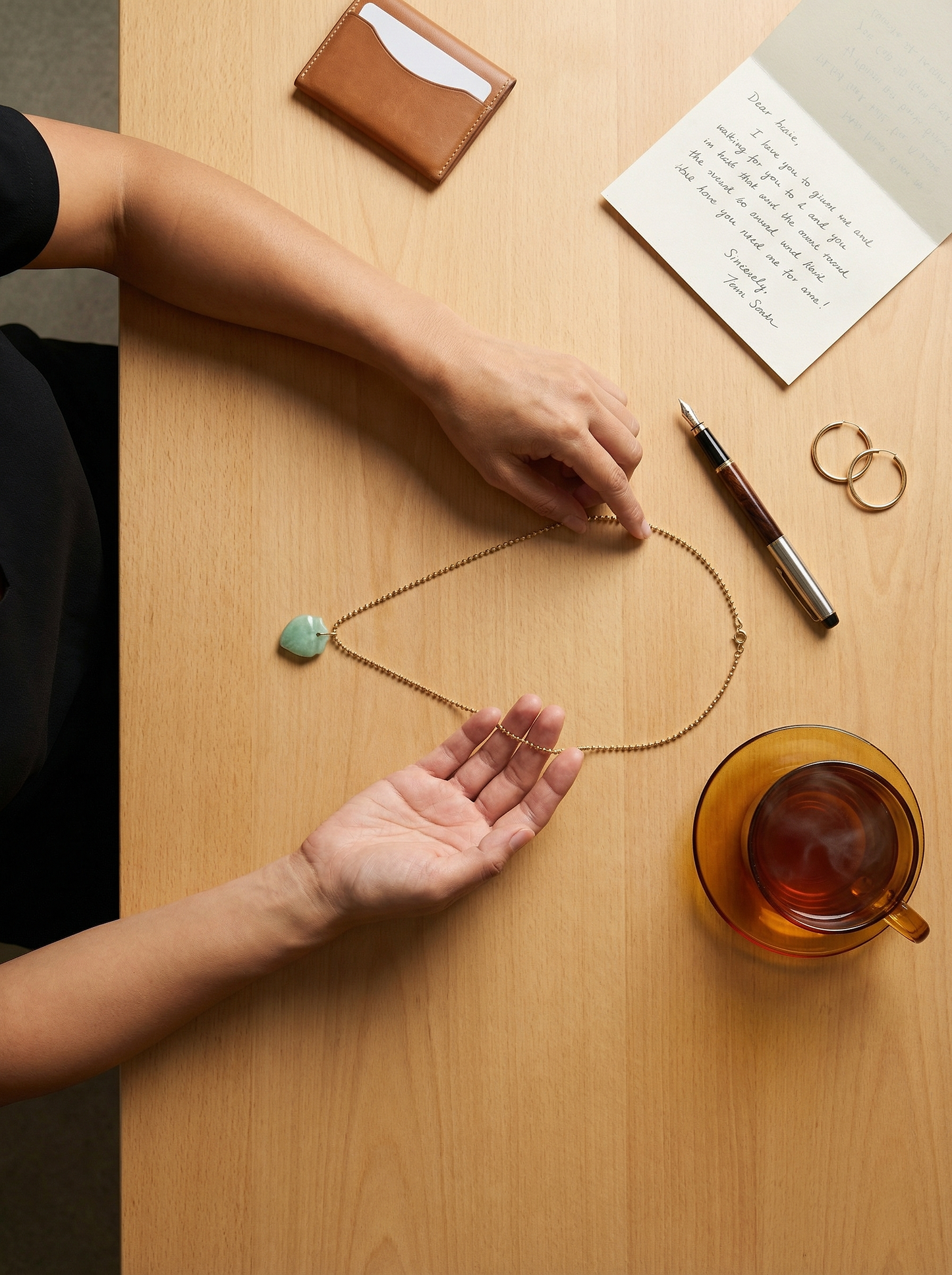 Overhead quiet table ritual with hands tracing gold ball chain among personal items.