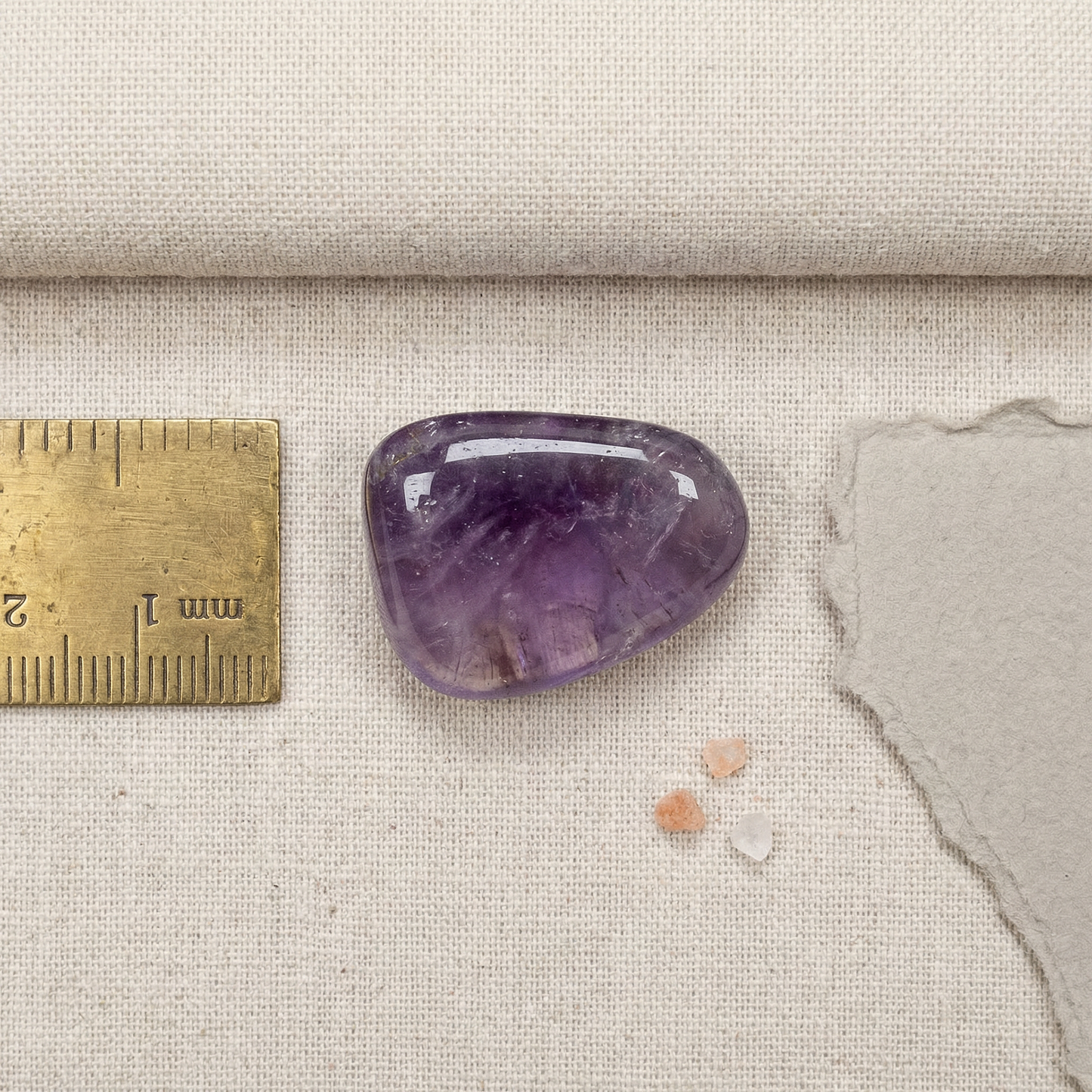 Tumbled amethyst on oat linen with brass ruler, deckle paper, and tiny salt grains