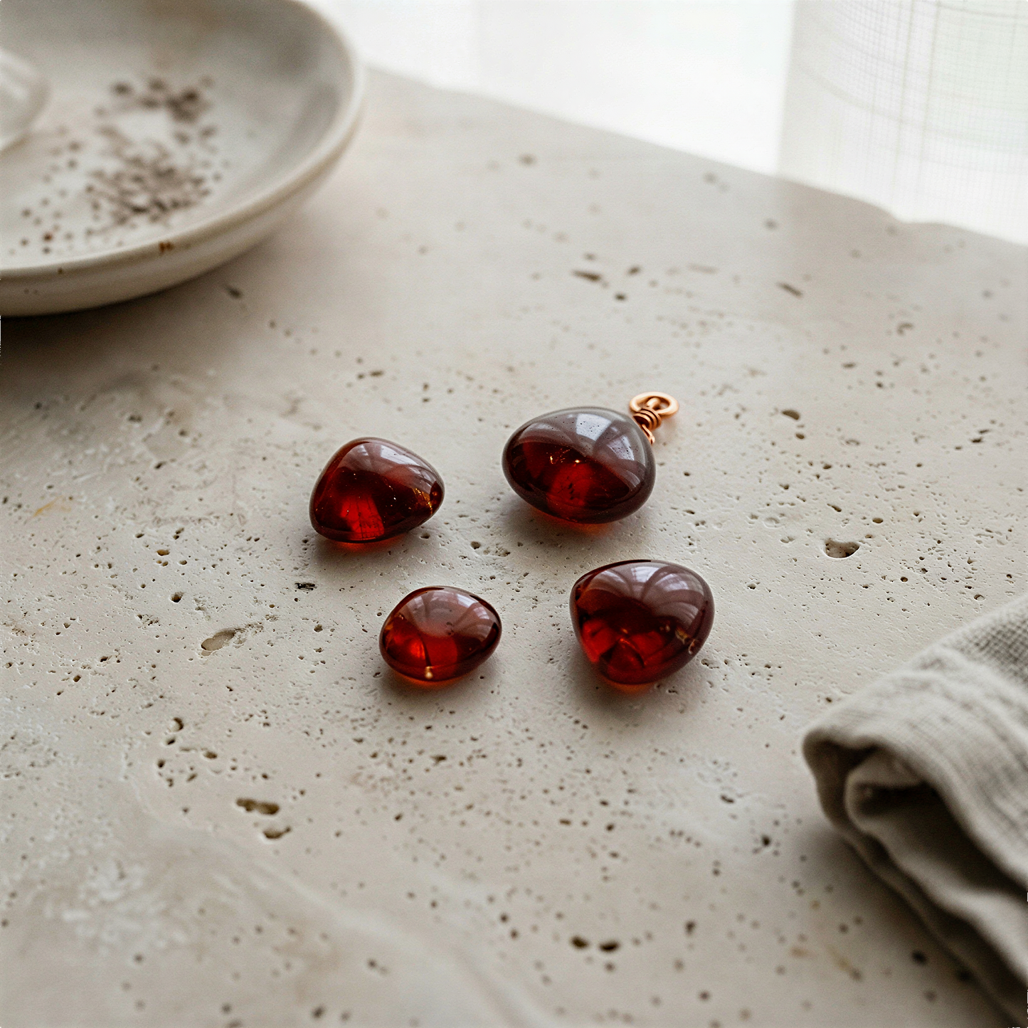 Smooth hessonite garnet heart briolette, tip-drilled, resting on pale stone with soft natural daylight.