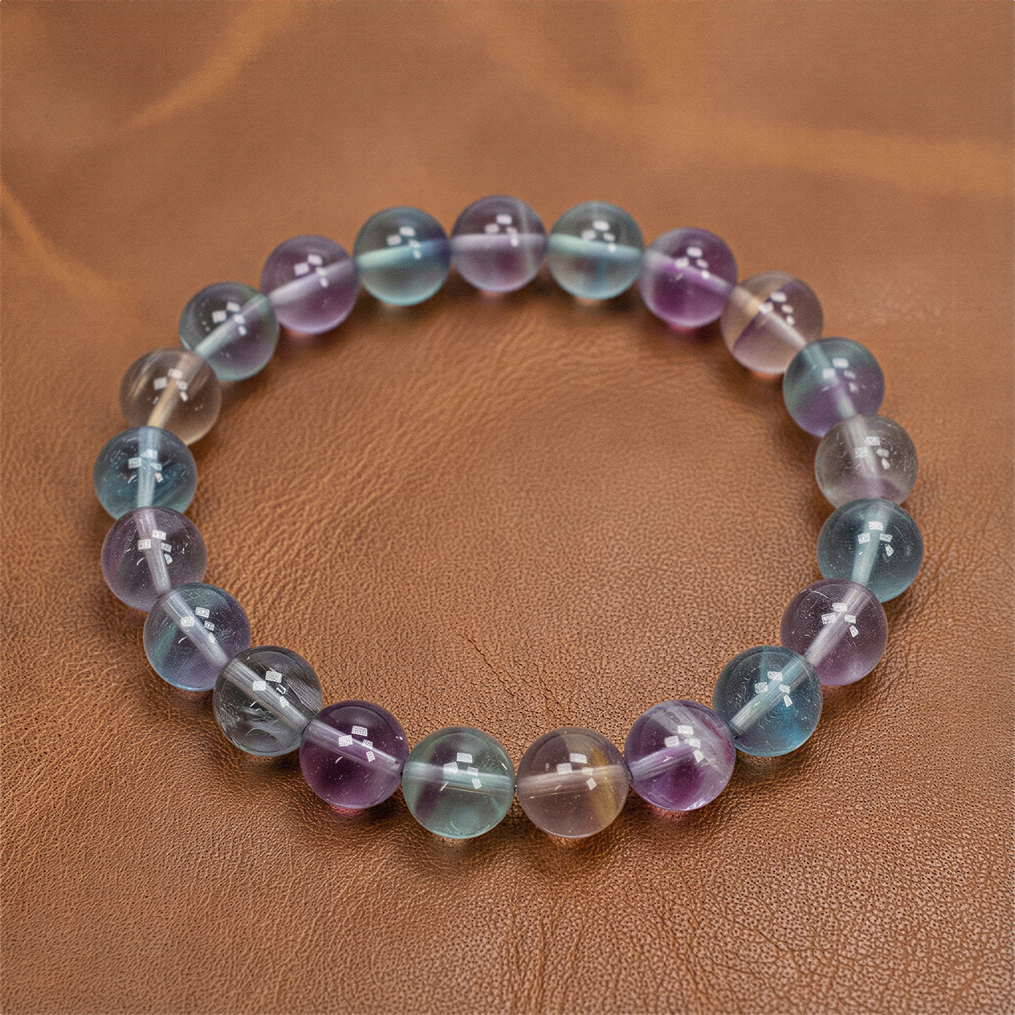 Rainbow fluorite stretchy bracelet with varied bead sizes resting on jade stone in soft, diffused light.