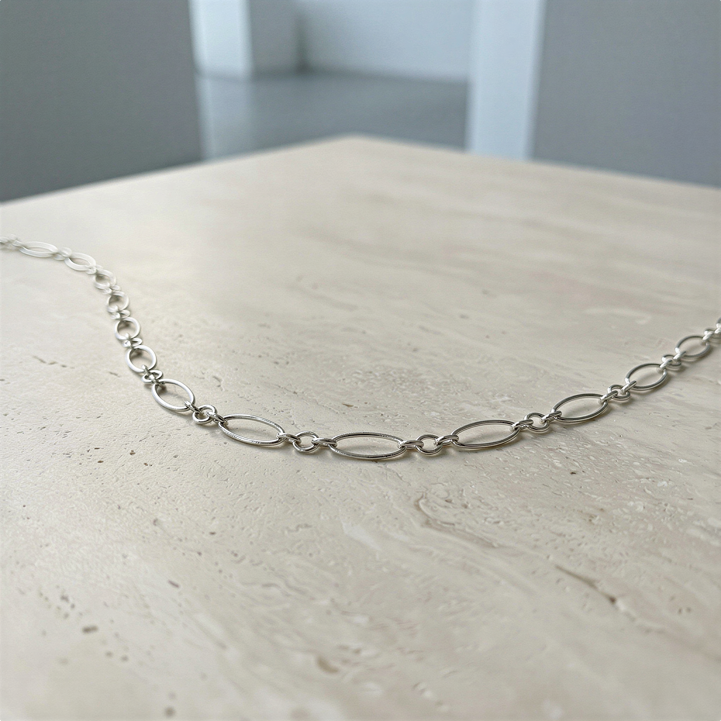 Sterling silver oval long and short chain arranged gracefully on soft neutral surface, serene light and refined balance