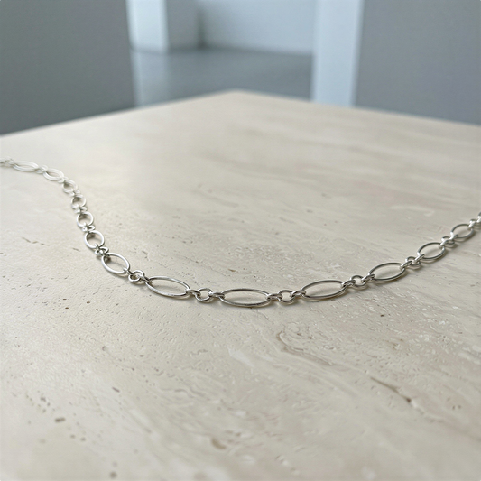 Sterling silver oval long and short chain arranged gracefully on soft neutral surface, serene light and refined balance