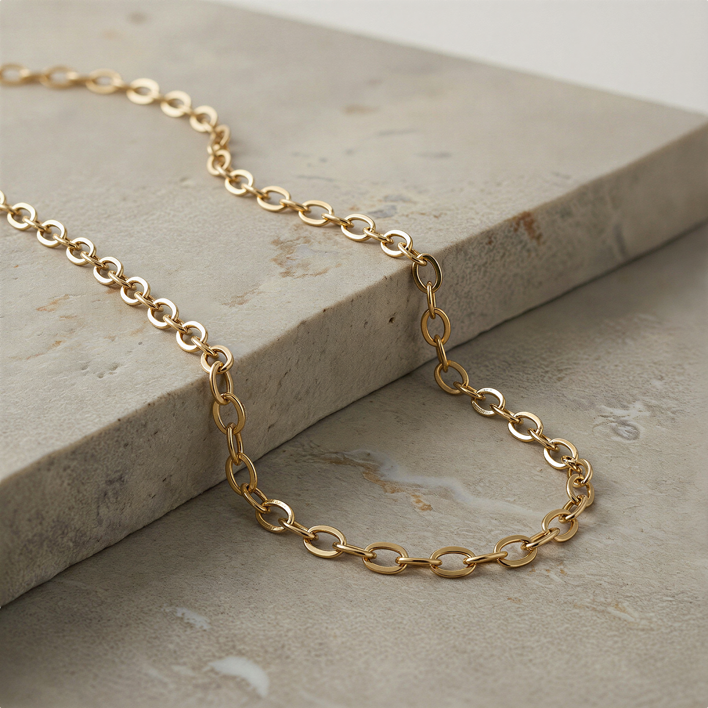 Gold fill flat cable chain resting on ivory silk with soft, balanced studio lighting.