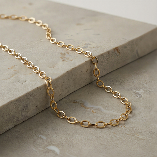 Gold fill flat cable chain resting on ivory silk with soft, balanced studio lighting.