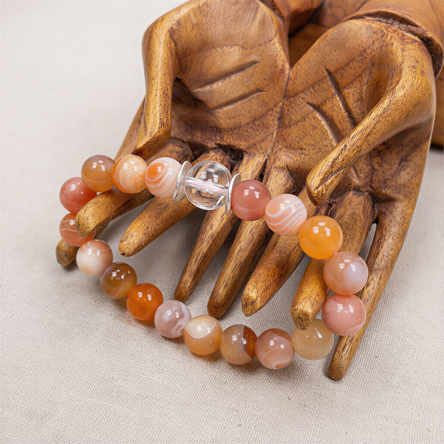 Cherry blossom stretchy bracelet kit displayed on a wooden hand, featuring agate beads and a clear quartz focal bead with delicate pink sakura blooms glowing inside soft studio light.