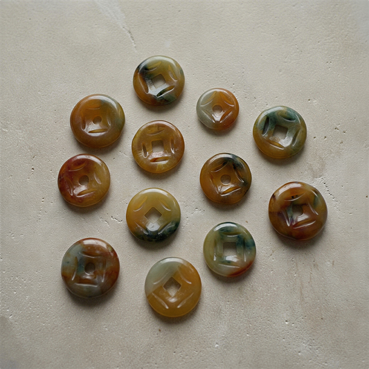 Jadeite carved donut coin charm resting on natural stone, soft daylight highlighting its serene translucence