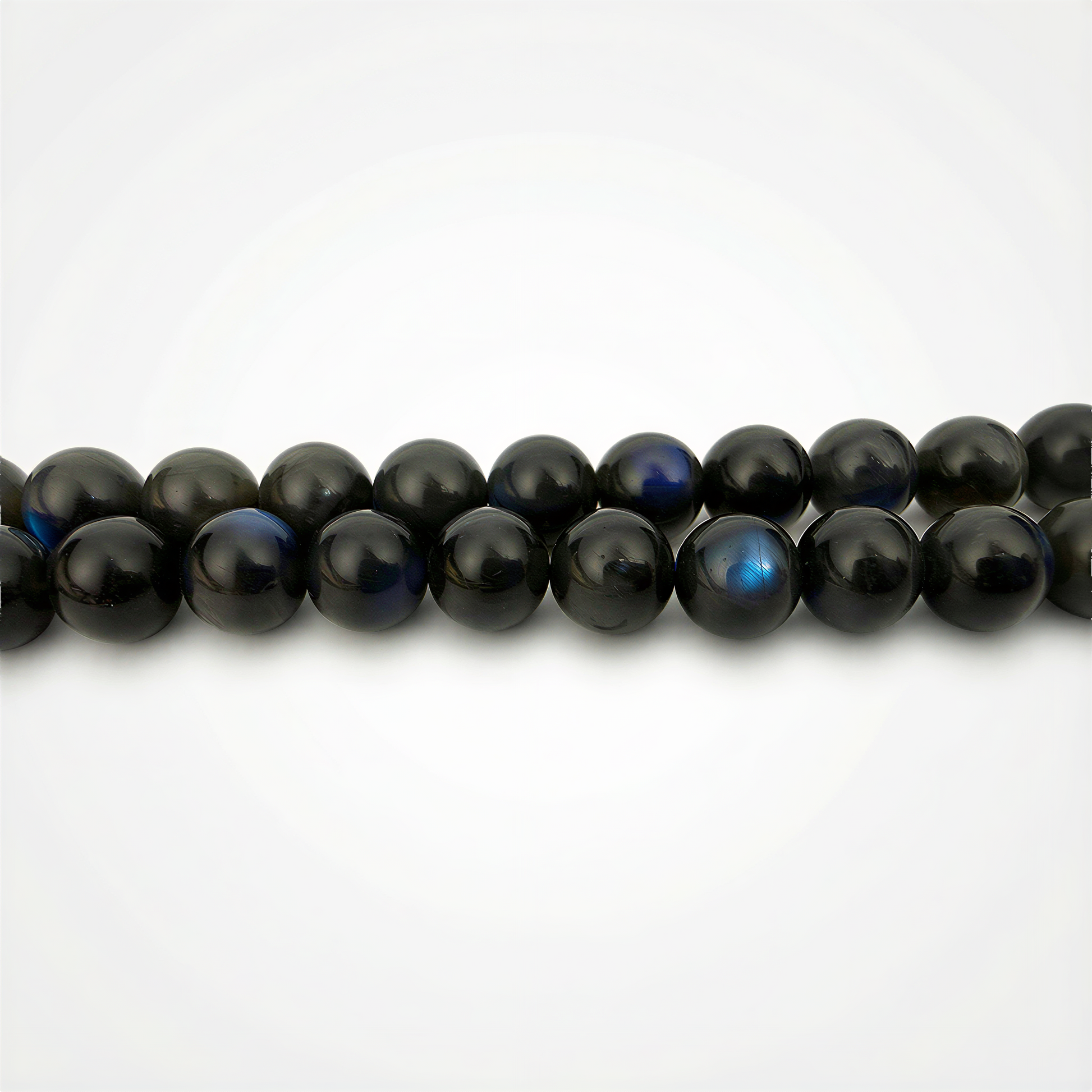 Smooth black labradorite round beads with subtle blue flashes, resting against a clean white background in soft, balanced studio light