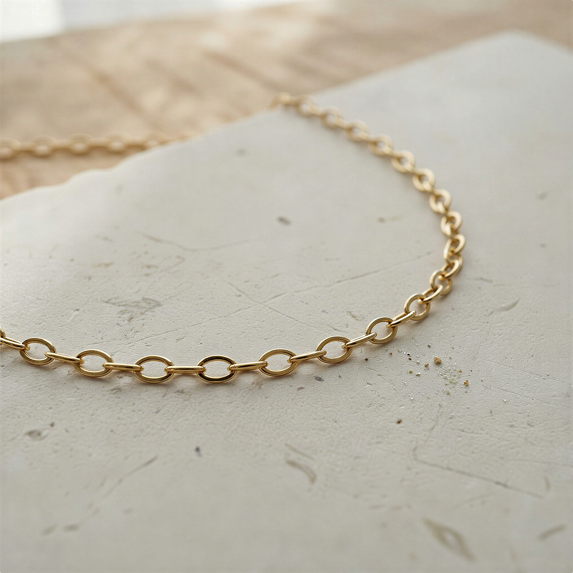 Silver and gold oval cable chain resting on natural stone with soft daylight