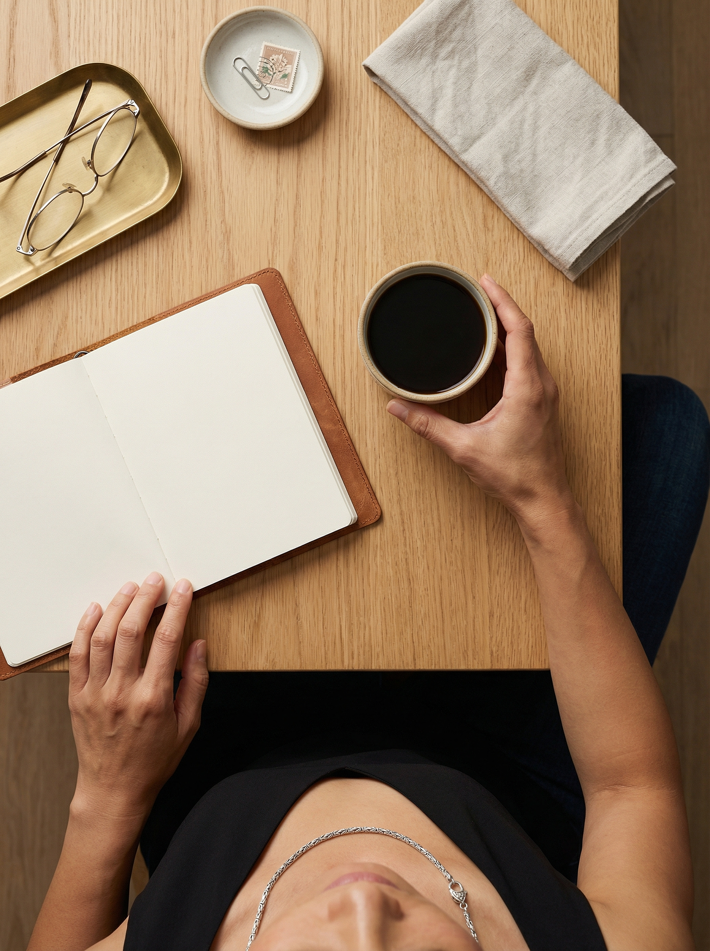 Overhead portrait of model seated at oak table wearing Byzantine silver chain, coffee and notebook nearby