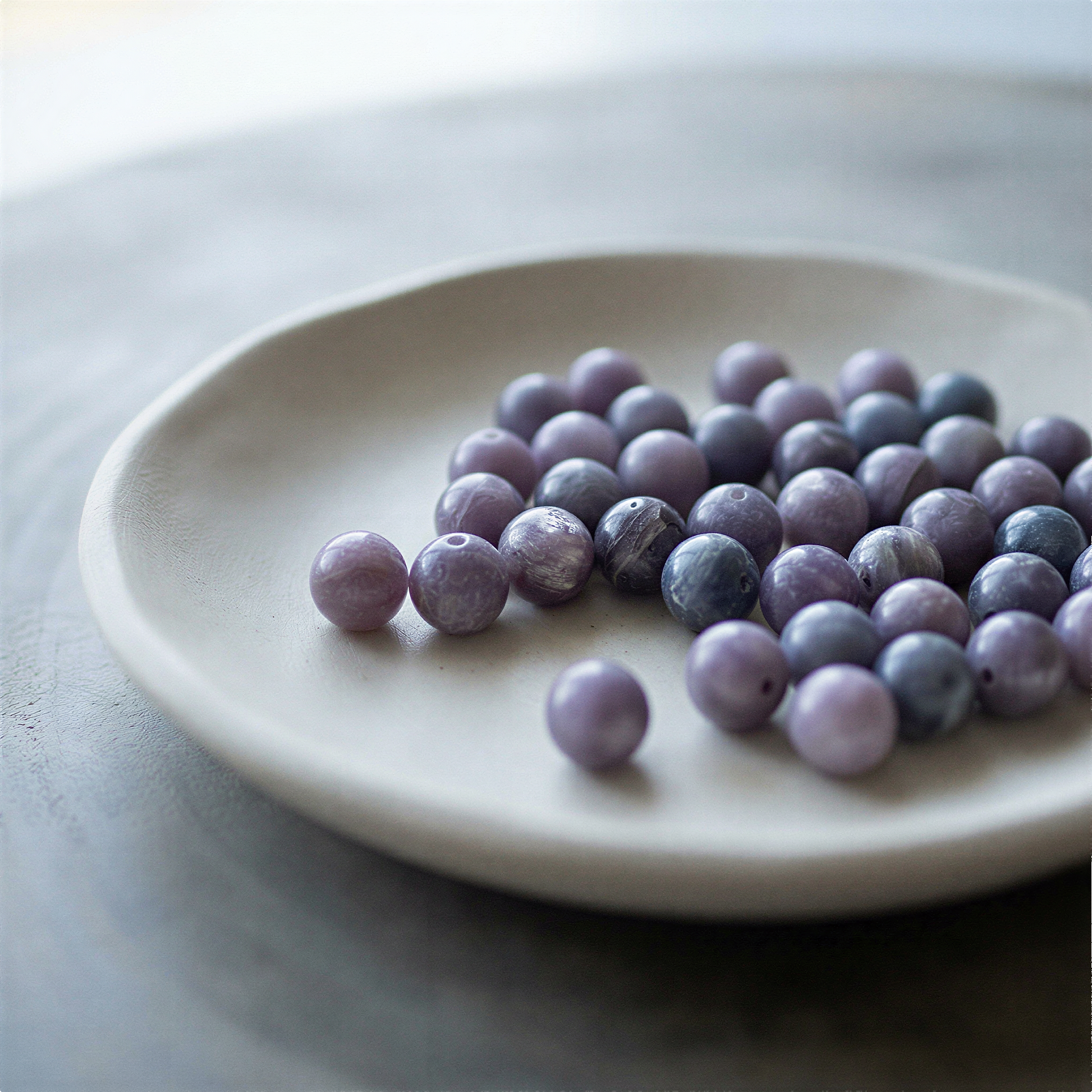 Single purple lepidolite 8mm bead resting on natural stone surface in soft, diffused daylight