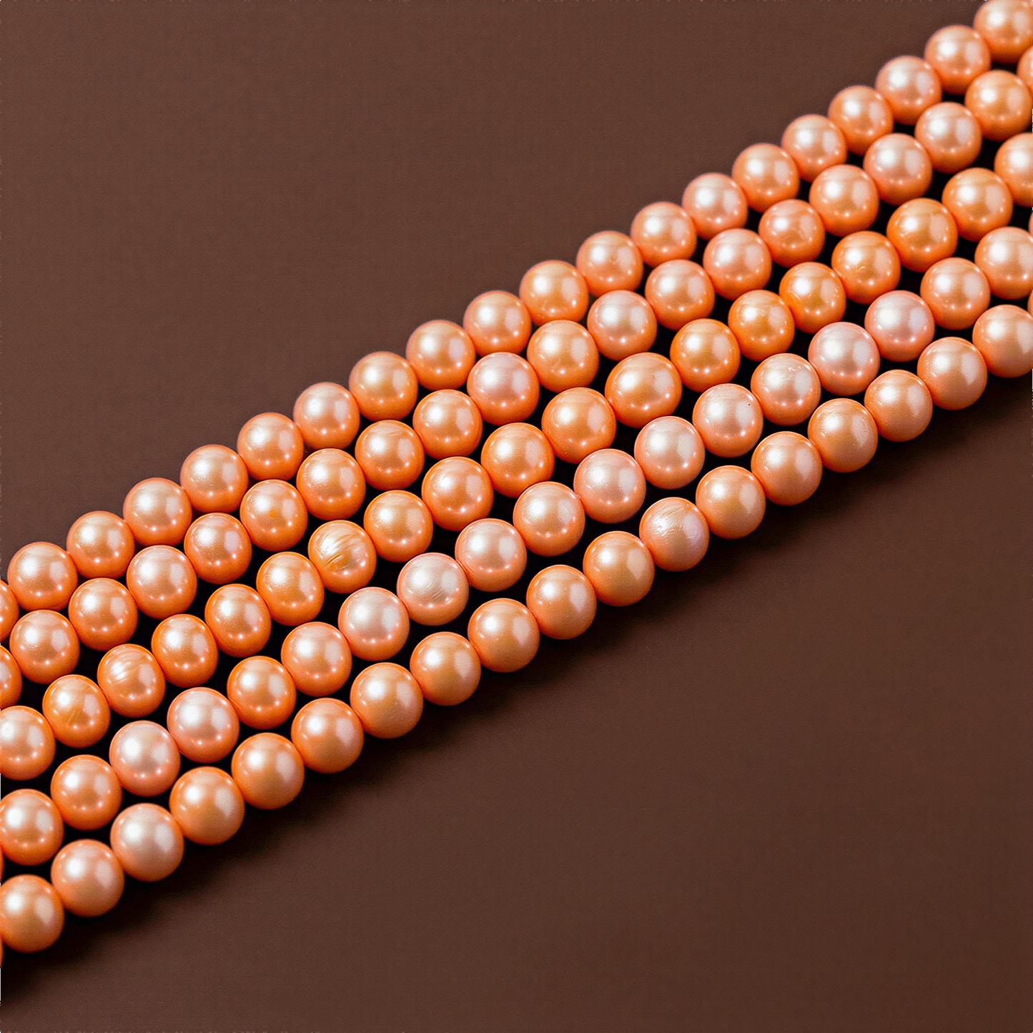 Small orange freshwater pearl strand resting against a warm chocolate-brown backdrop, softly lit to reveal natural luster and organic texture
