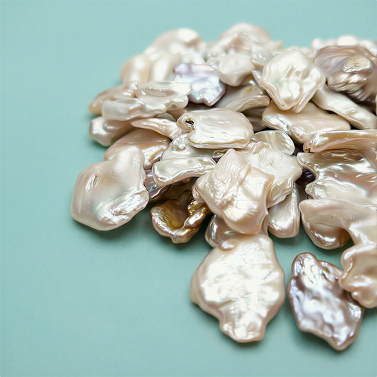 Four oversized baroque pearl beads glowing with natural iridescence, softly lit against a clean aqua backdrop that enhances their organic shapes and luminous texture.