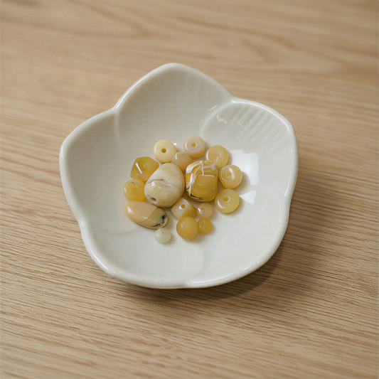 Golden yellow opal beads nestled in a white ceramic flower dish, resting on a softly lit natural surface with gentle, warm shadows.