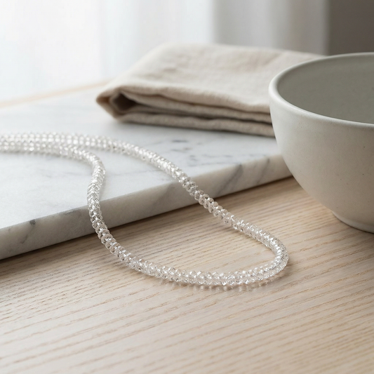 Herkimer quartz strand in soft morning light on honed marble and pale ash wood.