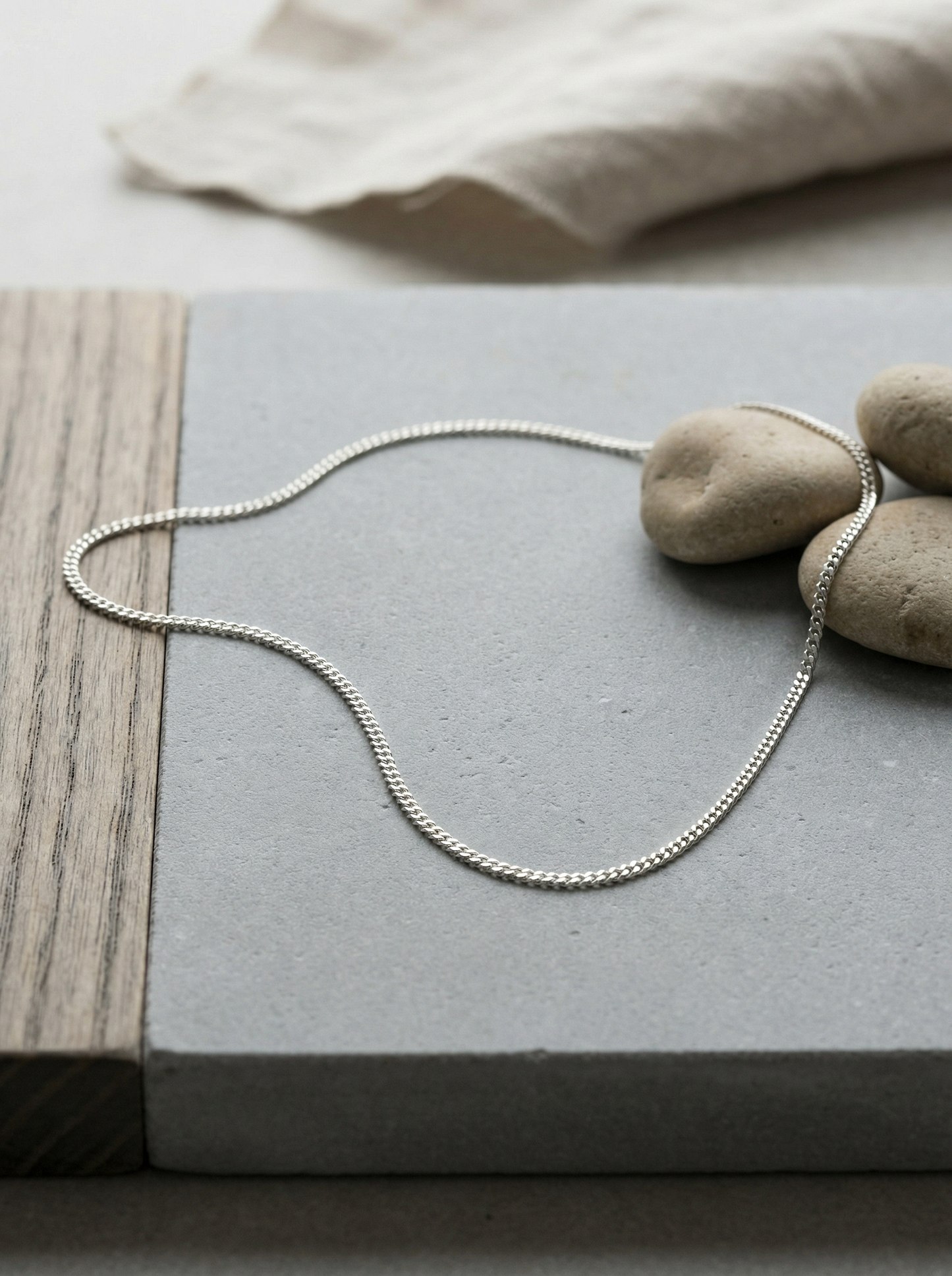 Sterling flat kerb chain on honed limestone with ash wood and linen vignette.