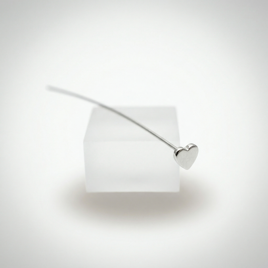 Sterling silver heart headpin floating on frosted pedestal in soft high-key light.