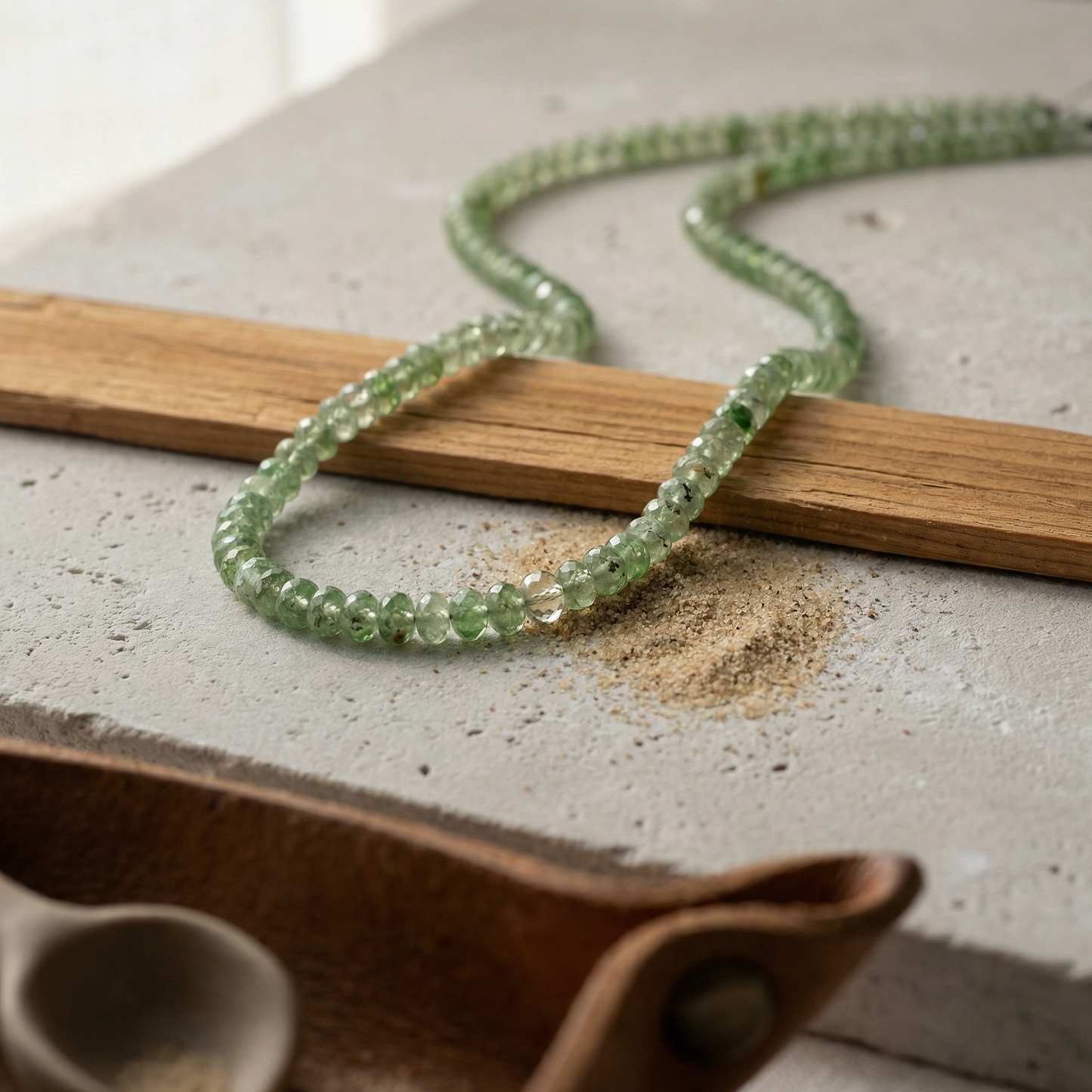 Graduated tsavorite rondelles on limestone slab with cedar strip and matte clay scoop.