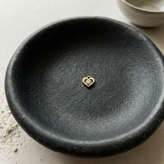 Gold-filled mini heart charm with subtle CZ crystal resting on natural stone in soft, diffused light