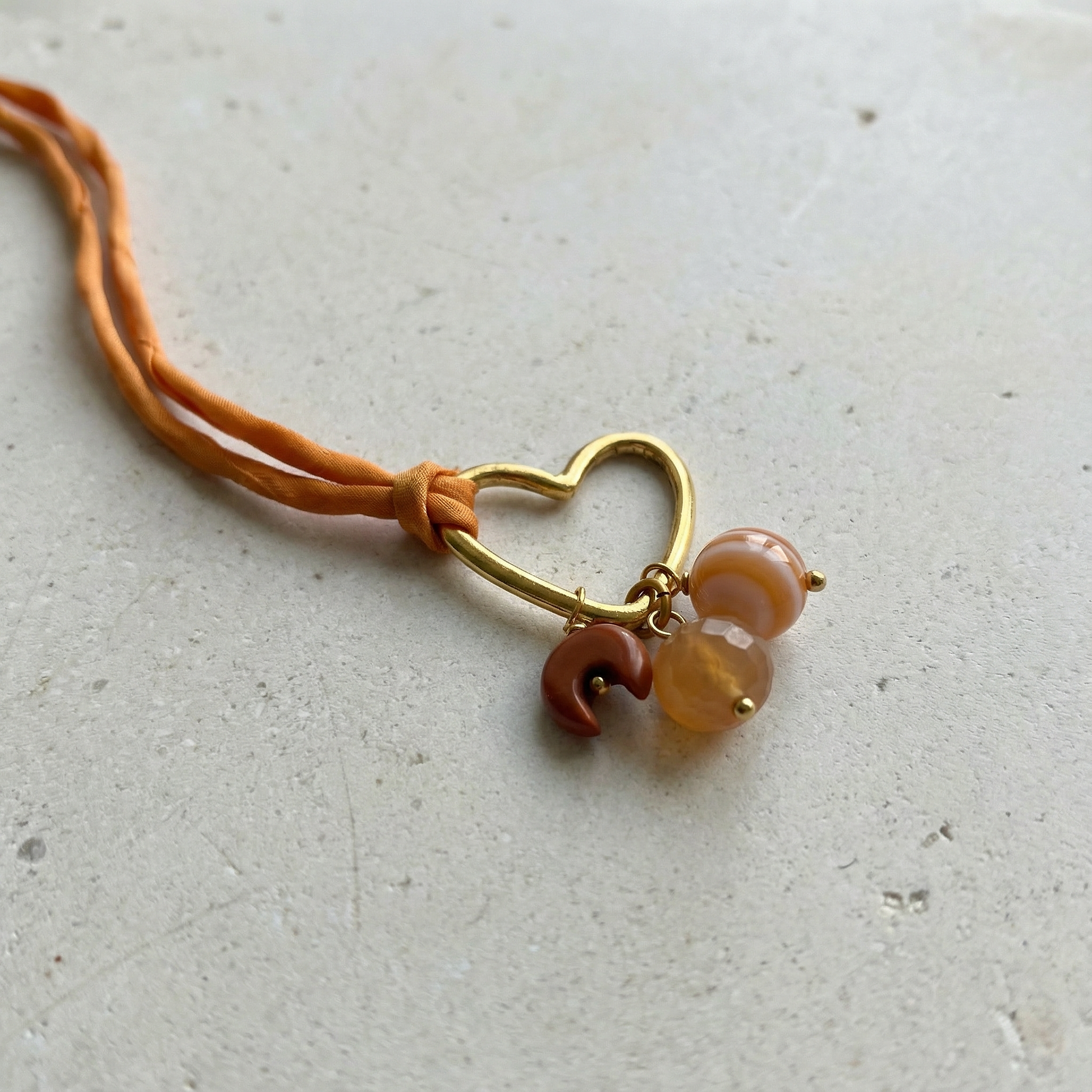 Heart-shaped plated hoop charm in silver and gold resting on sunlit stone with soft natural textures