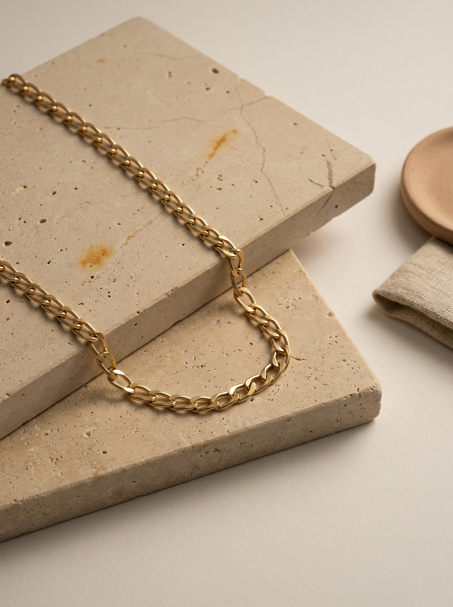 Gold cable chain draped over limestone slab with soft linen-filtered morning light.