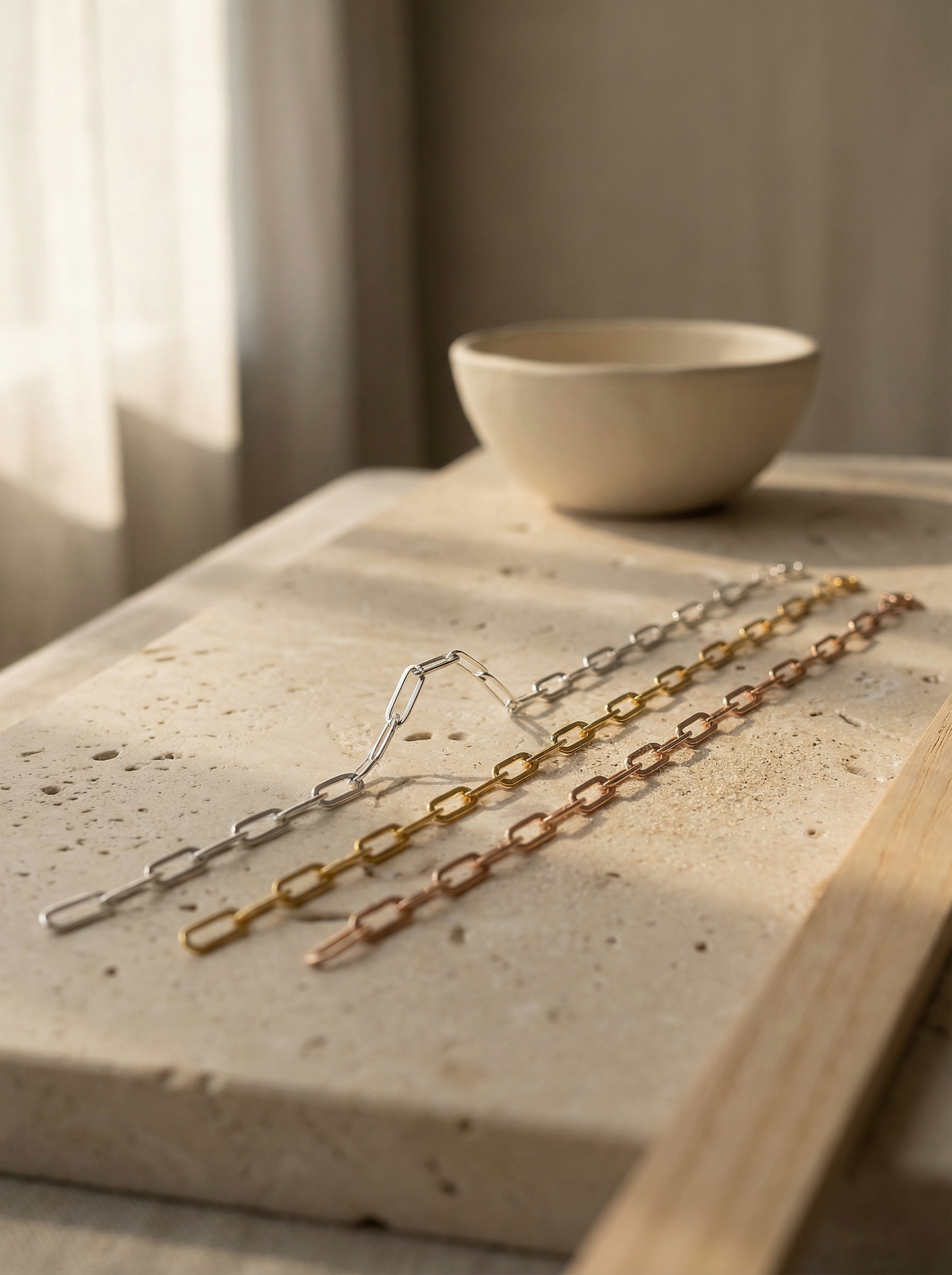Three flat paperclip chains on limestone ledge with linen background and soft morning light.