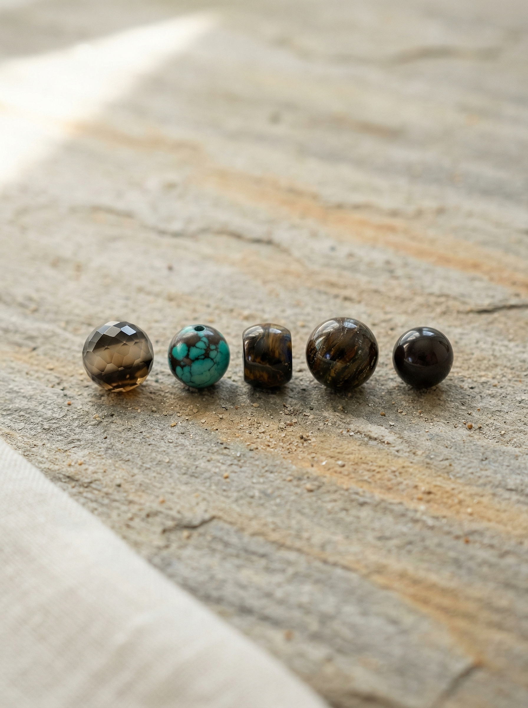 Five natural gemstone beads on weathered stone slab with soft morning light.