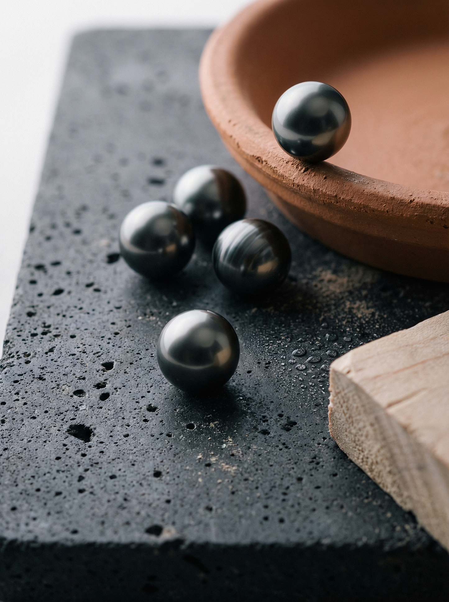 Single Tahitian pearl on honed graphite stone with terracotta bowl and maple board.