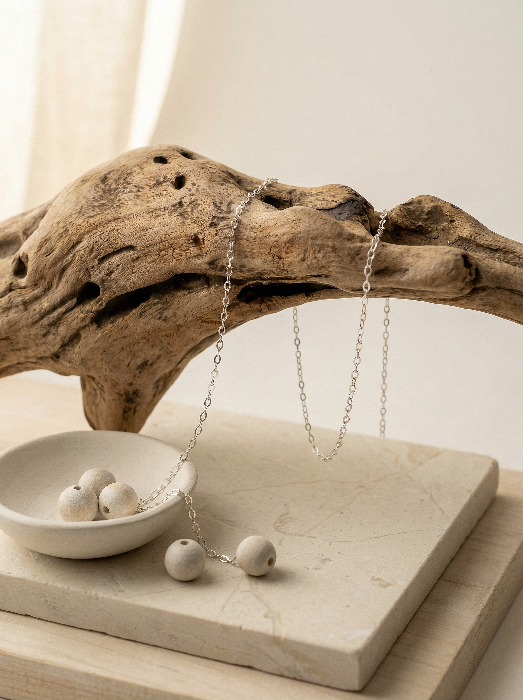 Sterling flat cable chain draped over driftwood on limestone with clay bowl and beads