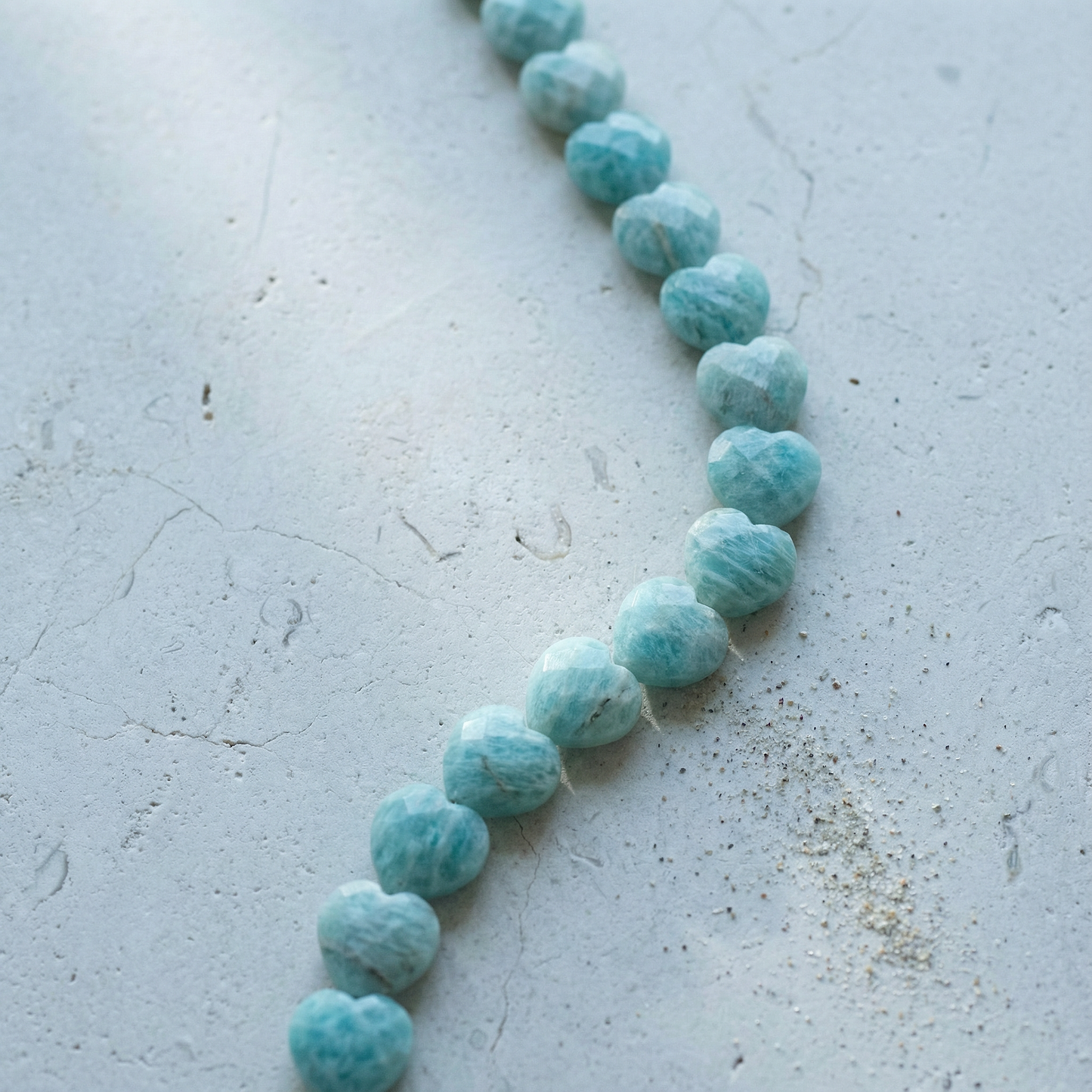 Faceted amazonite heart bead resting on natural stone surface with soft, diffused light and earthy tones