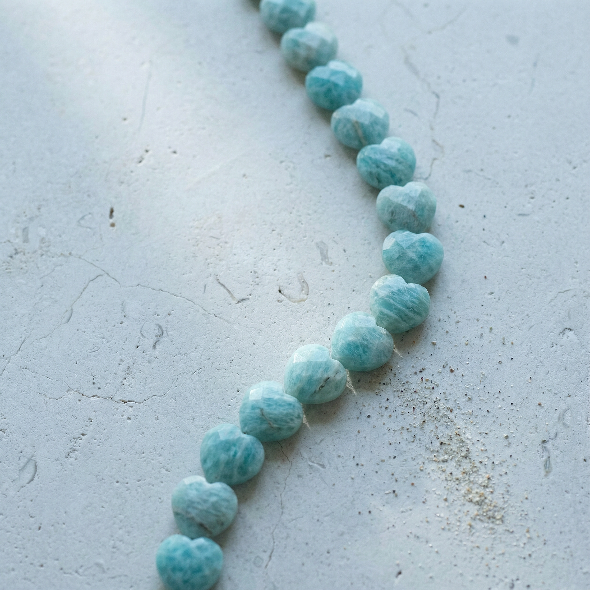 Faceted amazonite heart bead resting on natural stone surface with soft, diffused light and earthy tones