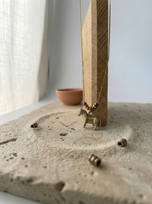 Antiqued brass horse pendant on pitted travertine with raw oak and terracotta bowl.