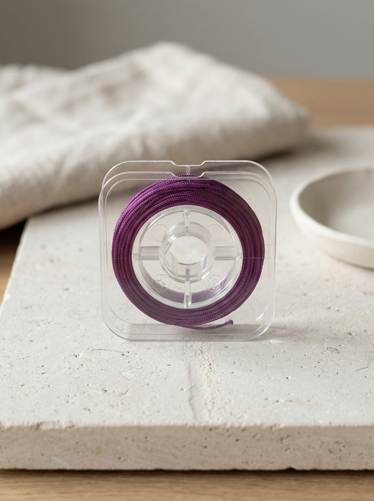 Single spool of purple Chinese knotting cord on pale limestone with linen backdrop.