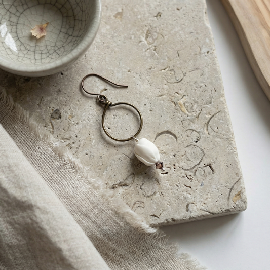 Pikake crystal hoop earring on worn limestone with linen and driftwood accents, soft daylight.