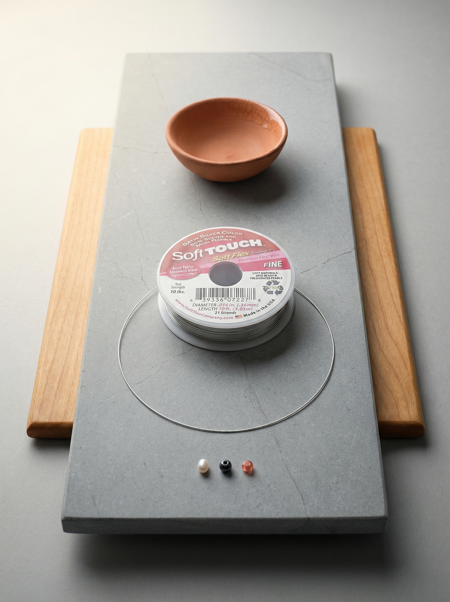 Soft TOUCH cable spool on honed limestone with maple, terracotta bowl, and three small beads.